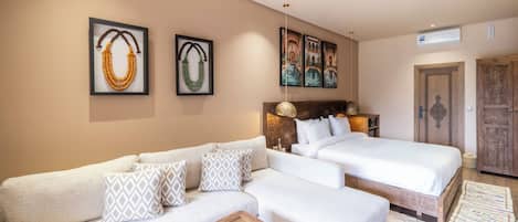 A hotel room with a sofa, two beds, a coffee table, and artwork on the walls.