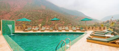 Une piscine entourée de montagnes, avec des chaises longues et des parasols.
