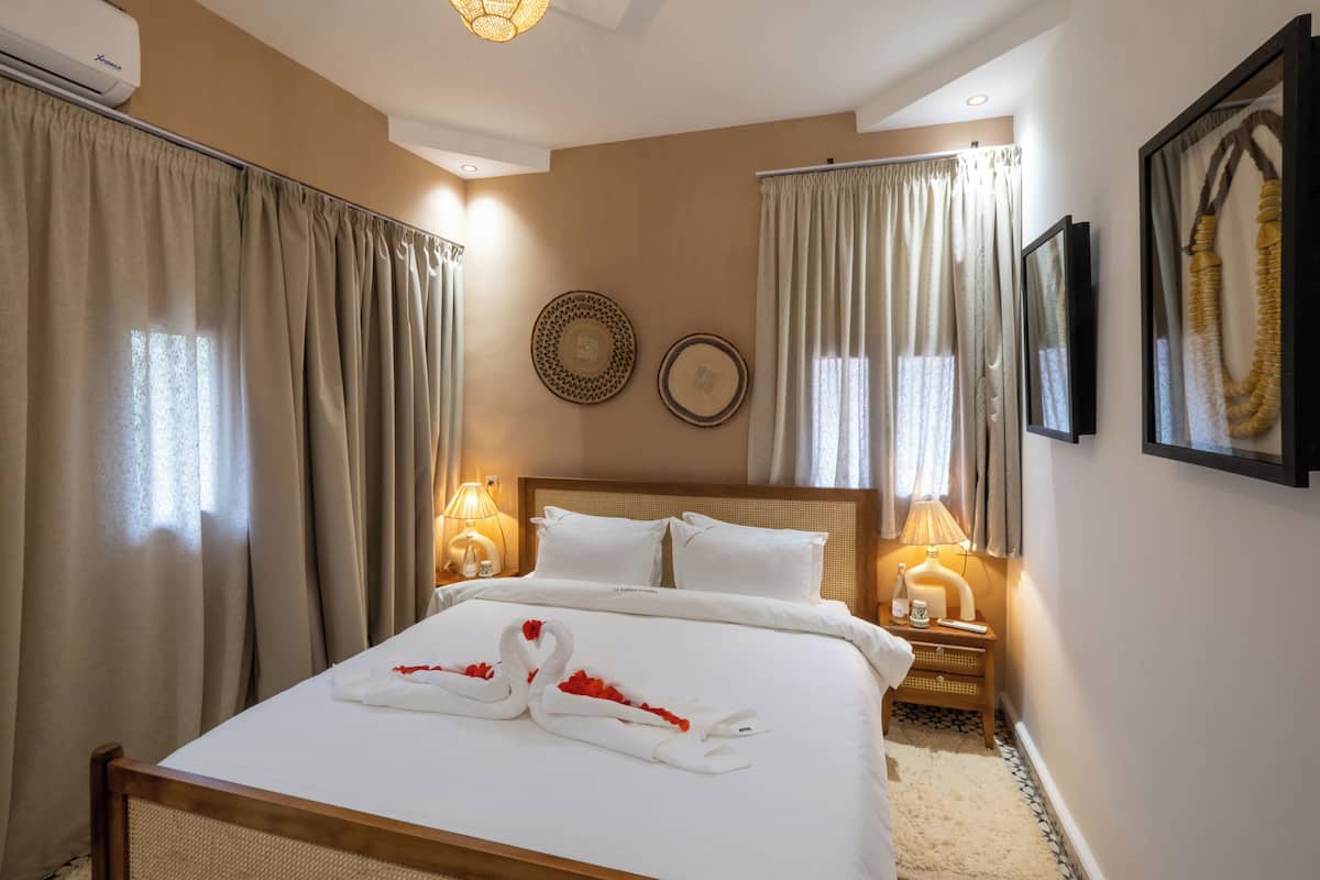 A hotel room with a bed, two bedside lamps, a headboard, a wall-mounted TV, and curtains.