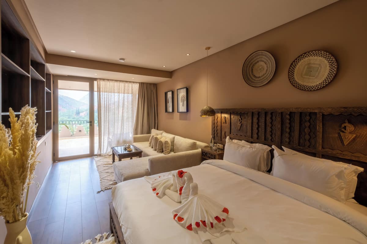 A hotel room with a large bed, a sofa, a dining table, and a view of the outdoors.