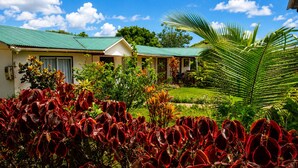 A building with a green roof, surrounded by lush greenery and red-leafed plants. - Cabañas Anariki - Cozy centrally located room with 2 single beds #2 (Hanga Roa)