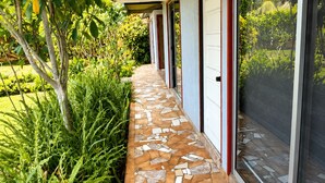 A covered walkway with a mosaic floor, flanked by greenery and leading to a building with large glass doors. - Cabañas Anariki - Cozy centrally located room with 2 single beds #2 (Hanga Roa)