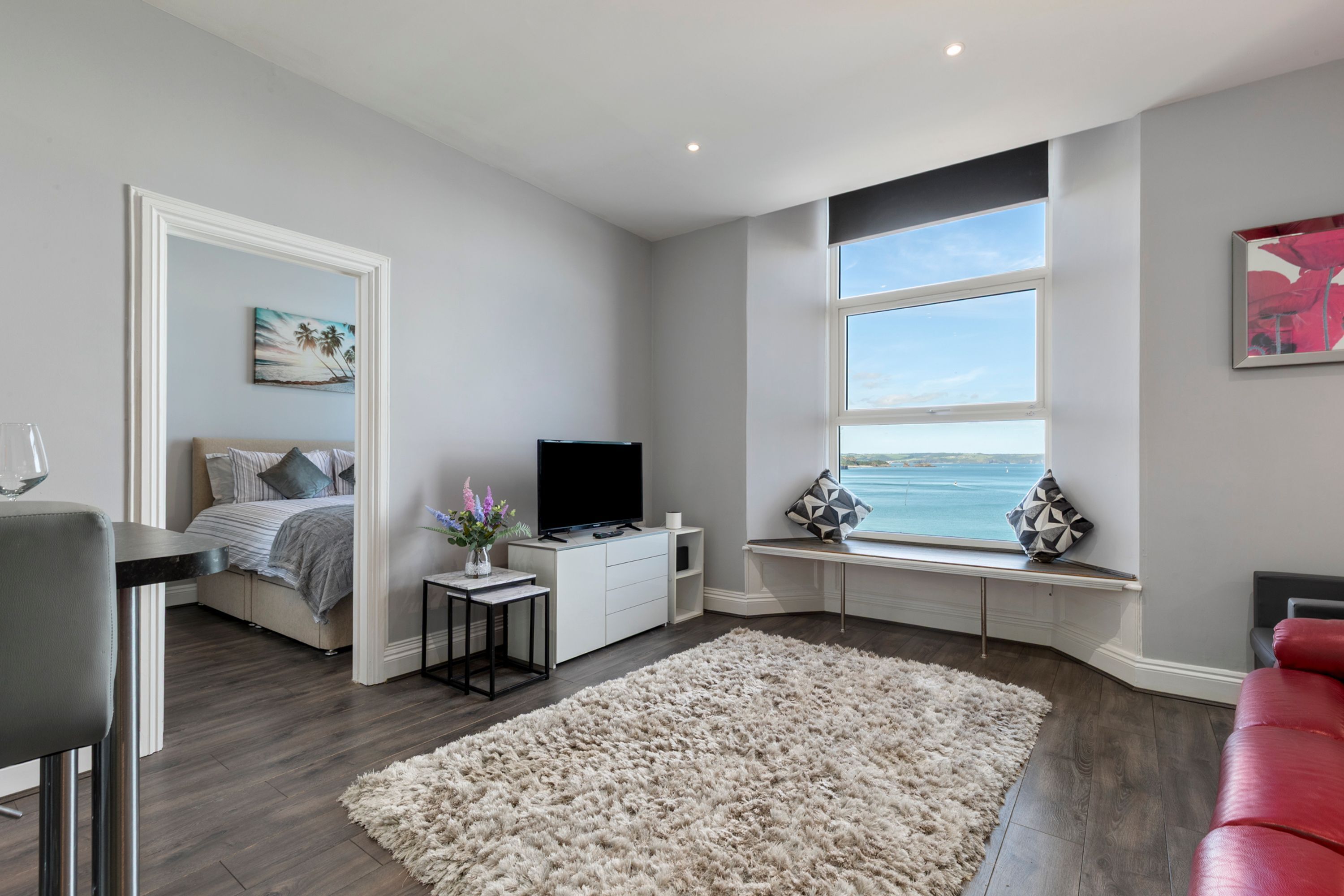 A modern living room with a large window, a flat-screen TV, a sofa, a coffee table, and a decorative rug.