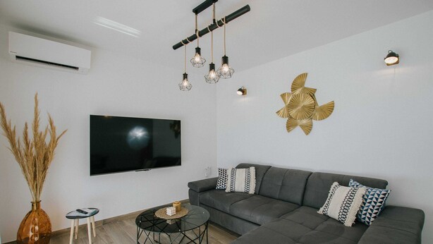 Ein modernes Wohnzimmer mit grauem Sofa, einem Flachbildfernseher, einer Wanddekoration und einer besonderen Pendelleuchte.