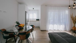 Eine moderne Küche mit weißen Schränken, einem Esstisch mit Stühlen und einer Wohnbereits mit einer Couch und einer Vase.