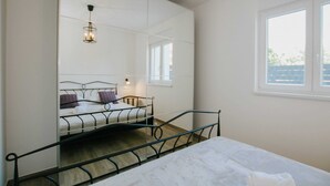 Ein Schlafzimmer mit Bett, Fenster, Spiegel und einer Pendelleuchte.