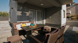 Eine Terrasse im Freien mit Korbmöbeln, einem Glastisch und einer Schiebetür.