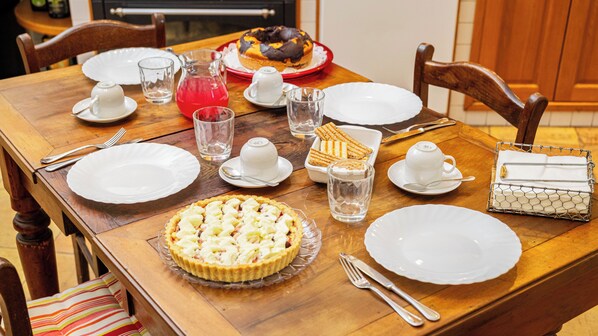 Una mesa de madera dispuesta con platos, cubiertos, vasos, una jarrón, un pastel y un bizcocho.