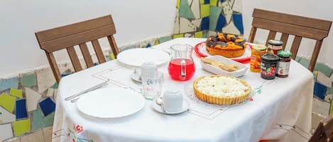 A table set for a meal with plates, cutlery, a pie, a pitcher of red liquid, and jars of preserves.
