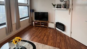 A modern living room with a large TV, a fireplace, and a view of the city through large windows. - Apartment Sleeps 6 With Air Conditioning (Manchester)