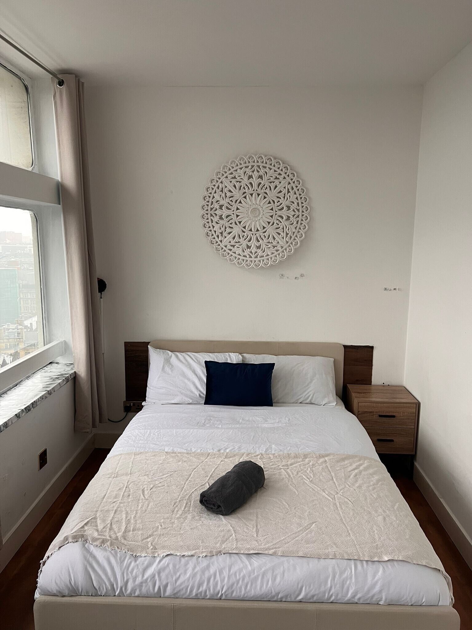 A bedroom with a bed, a nightstand, a wall decor, and a window.