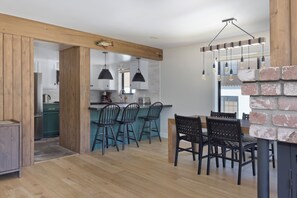 Eine moderne Küche mit Holzbalken, einem Essbereich mit schwarzen Stühlen und einer Wand mit Ziegelakzenten.