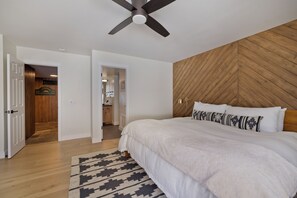 Ein Schlafzimmer mit einem großen Bett, einem Deckenventilator, Holzvertäfelung an der Wand und einem gemusterten Teppich.