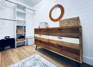 A modern room with a wooden dresser, open shelving, a mirror, and a woven basket. - Sabine 1E Couples Getaway Freshly Remodeled- Brand New Everything! (Pensacola Beach)