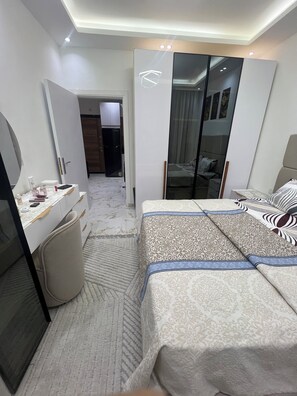 A modern bedroom with a bed, a desk, a mirror, and a wardrobe. - La bela resort apartment (Red Sea Governorate)