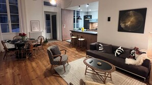 Un salon moderne avec un canapé, une table à manger et des chaises, une cuisine en arrière-plan et une grande fenêtre.