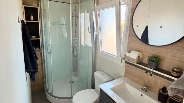 Ein kleines Badezimmer mit einer Duschkabine, Toilette, Waschbecken und einem Spiegel.