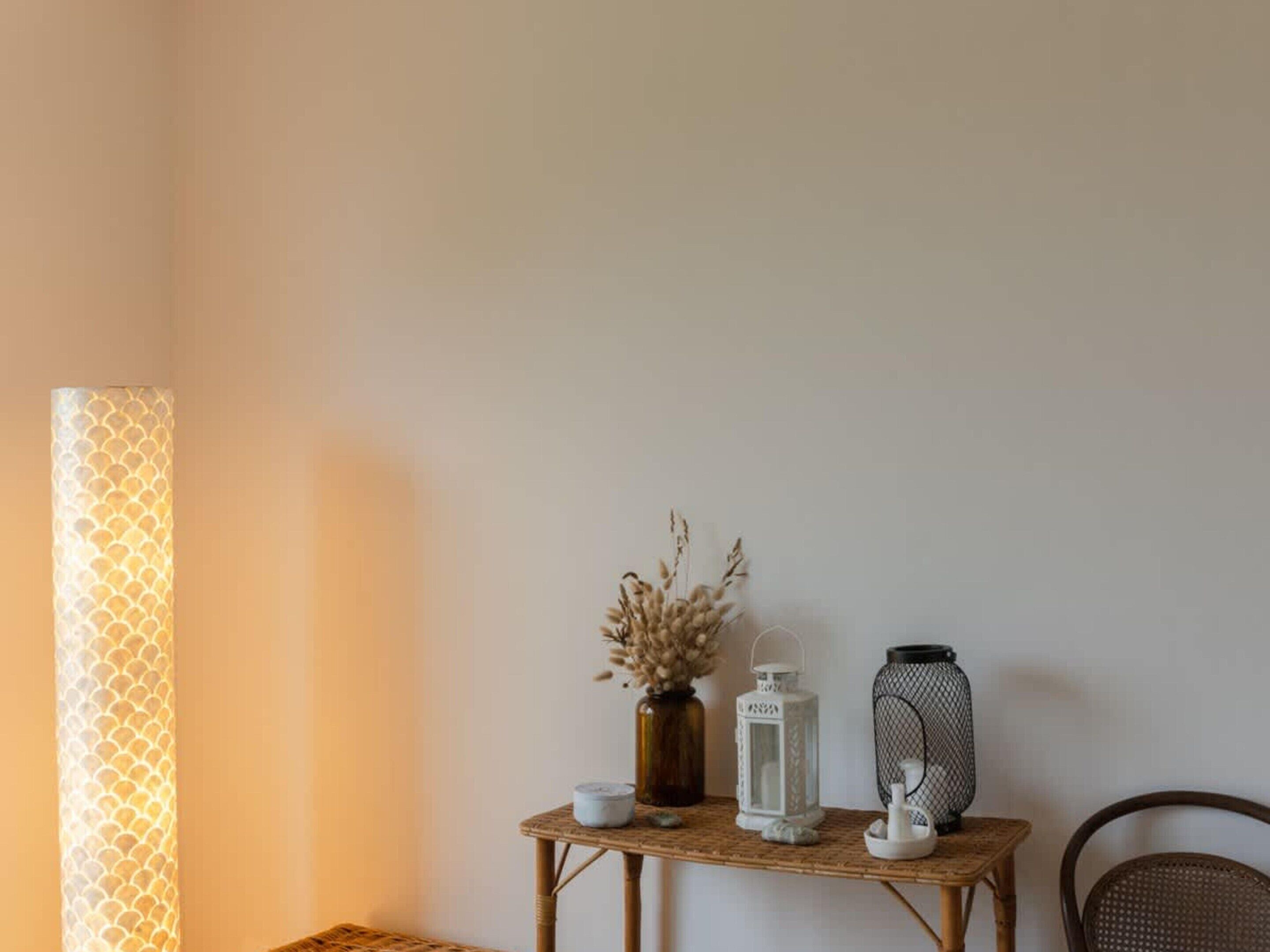 A room with a woven table, a tall lamp with a patterned shade, and two decorative items on the table.
