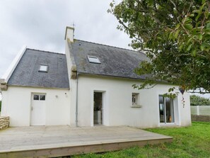 A two-story white house with a sloped roof, a wooden deck, and a tree in the foreground. - House by Plage de Melon With Garden Retreat (Porspoder)