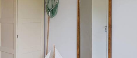 A room with a white wardrobe, a green net, a wooden sailing ship model, a large mirror, and a wicker chair.