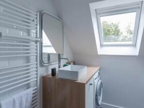 A modern bathroom with a built-in towel rack, a sink, a mirror, a window, and a washing machine. - House by Plage de Melon With Garden Retreat (Porspoder)
