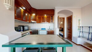 Cocina compacta con armarios de madera, horno empotrado, microondas y pileta.