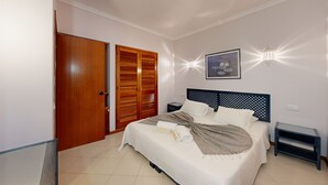 Un dormitorio con cama, armario de madera, mesita de noche, lámpara de pared y un cuadro enmarcado.