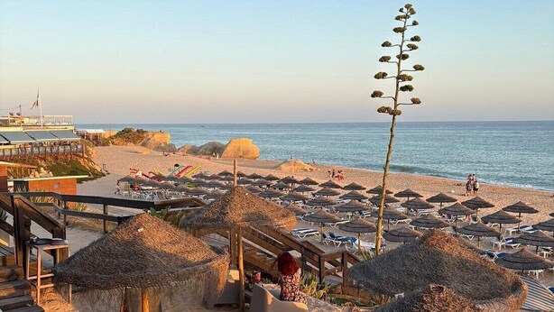 Ein Strandresort mit Reetdachschirmen, Liegestühlen und einem Holzdeck mit Blick auf das Meer.