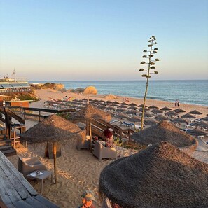 A beach resort with thatched umbrellas, lounge chairs, and a wooden deck overlooking the sea. - Villa Hipolito, 4-Bedroom, Praia da Galé (Albufeira)
