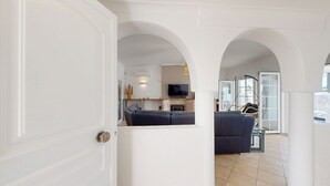Ein offenes Durchgangsbild zu einem Wohnbereich mit Sofa, Fernseher und einer Hängematte.