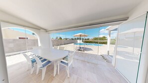 Un patio moderno al aire libre con una mesa y sillas de comedor, una piscina y una vista despejada del paisaje circundante.