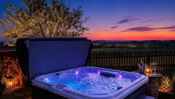 Un jacuzzi con cubierta de madera, cerca de madera y vista al atardecer.