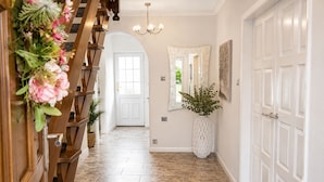 Un pasillo con una escalera de madera, una puerta blanca grande, un espejo y una planta en maceta.