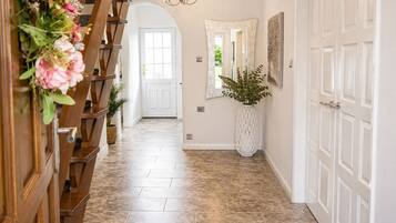 A hallway with a wooden staircase, a large white door, a mirror, and a potted plant.