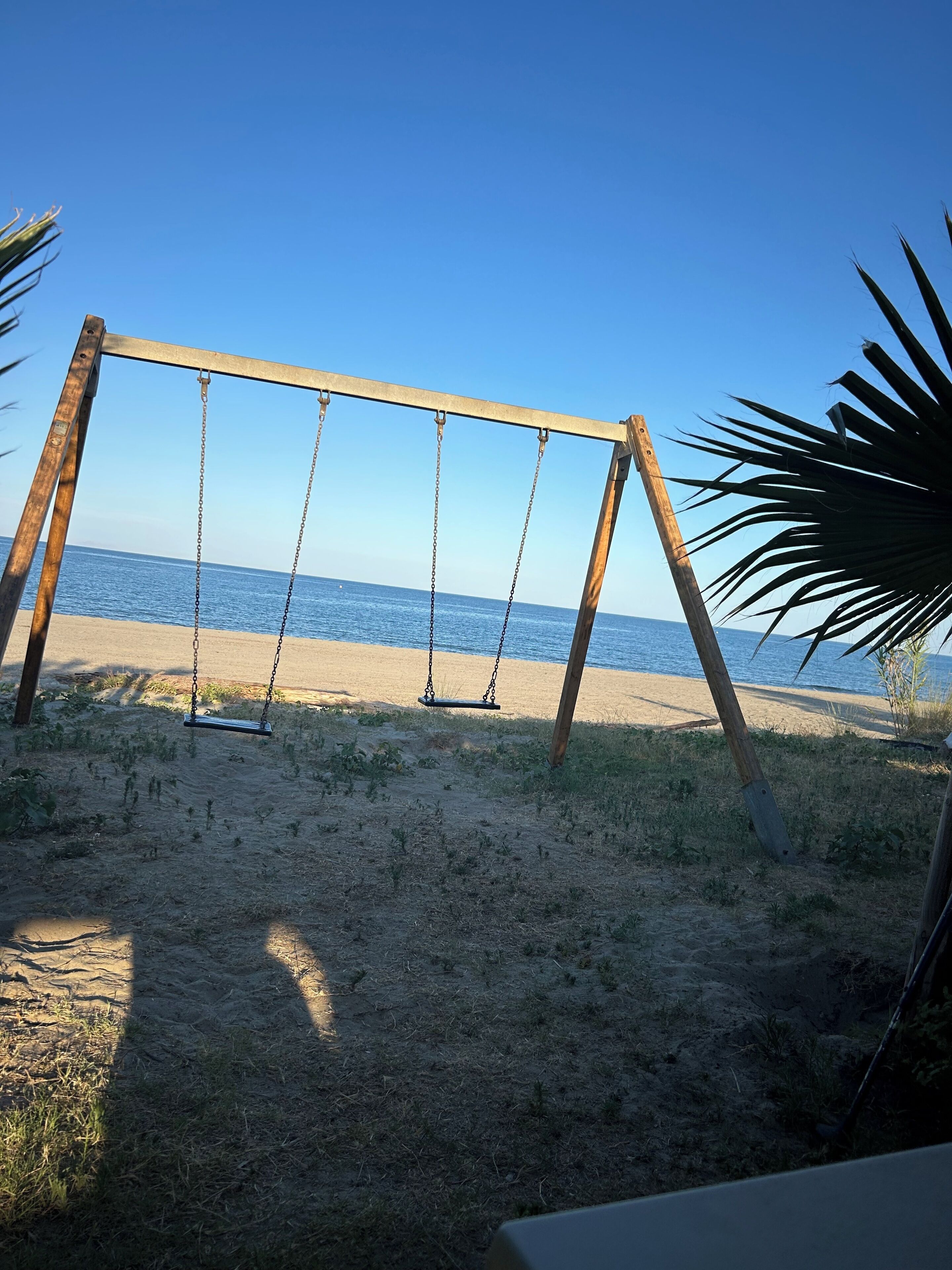 Un conjunto de columpios de madera sobre una playa arenosa, con vistas despejadas al océano.