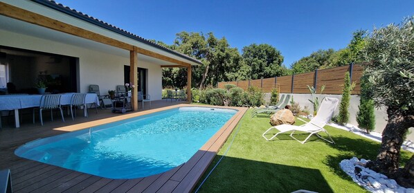Un jardin avec une piscine, un patio couvert et une pelouse agrémentée d’un fauteuil de relaxation.