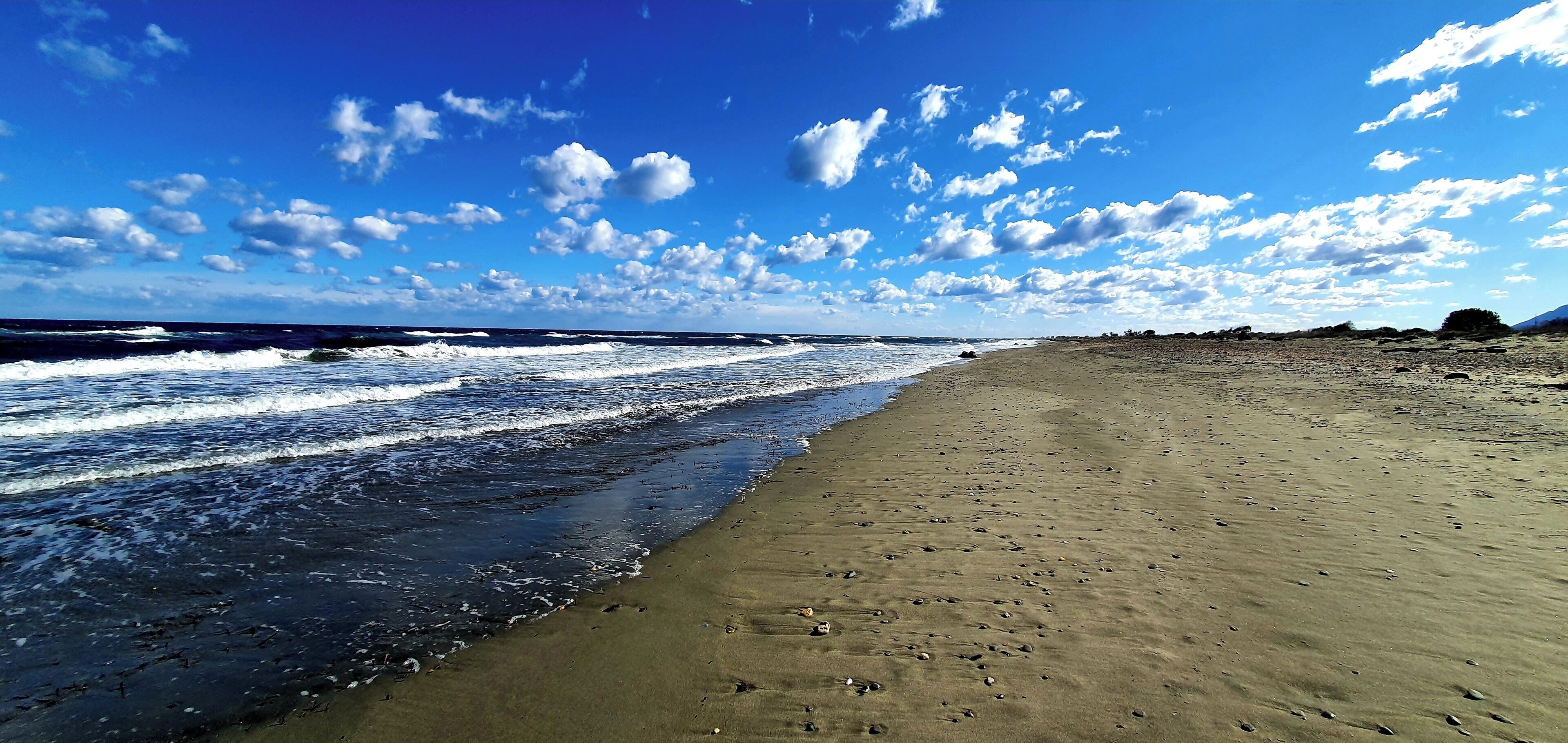 Een strand met golven, een heldere lucht en een berg in de verte.