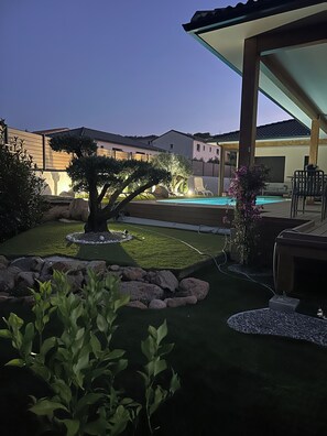 Ein Garten mit Schwimmbecken, überdachter Terrasse und gepflegtem Rasen.