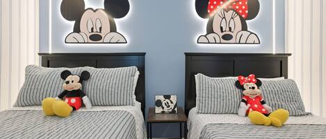 Two beds with Mickey Mouse and Minnie Mouse wall art, a nightstand with a Mickey Mouse picture, and striped bedding.