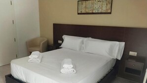 Ein Hotelzimmer mit einem großen Bett, einem Sessel, einem Nachttisch und einem an der Wand befestigten Kunstwerk.
