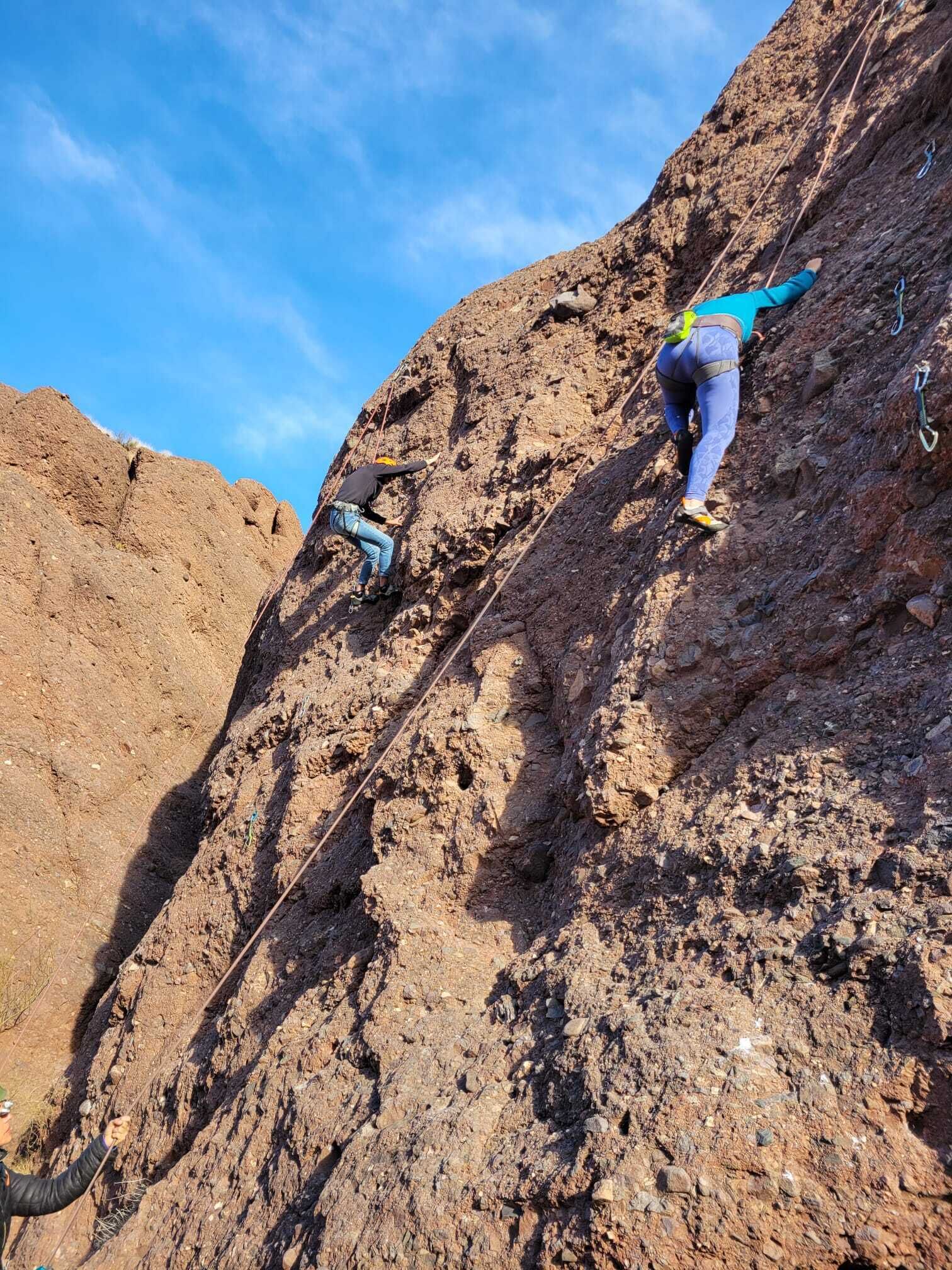A person climbing a rocky cliff with climbing gear.