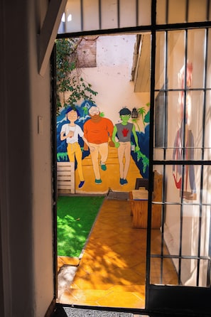 Un pasillo con piso de baldosas, una pared blanca y una puerta con reja metálica.