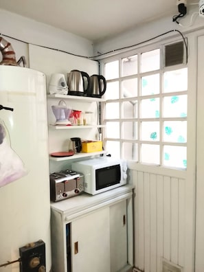 Cocina compacta con microondas, tostadora y hervidor sobre una pequeña encimera.