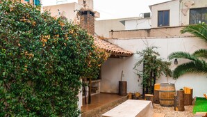 A rooftop patio with a table and benches, surrounded by greenery and a swimming pool.