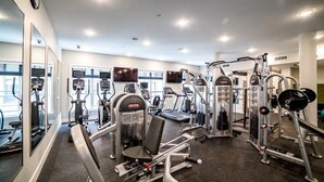 Ett gym med olika träningsmaskiner, speglar och en klocka på väggen.