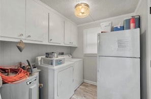 Una cocina compacta con muebles blancos, lavadora, refrigerador y una lámpara en el techo.