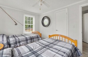 A bedroom with two beds, a ceiling fan, a window with blinds, a door, and a wall-mounted circular object.