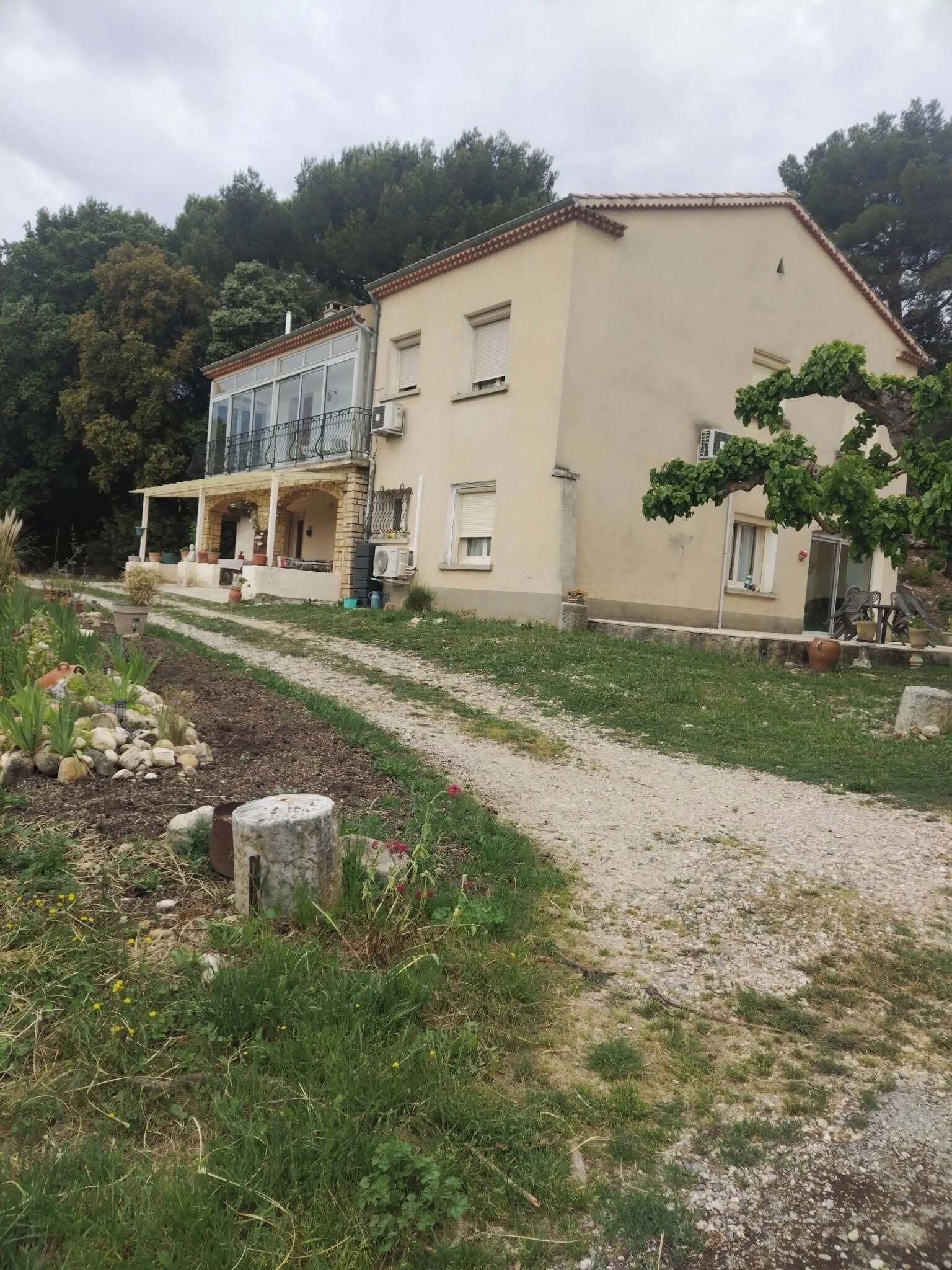 Un bâtiment à deux étages doté d’un balcon, d’un jardin avec un chemin de gravier et d’un arbre.
