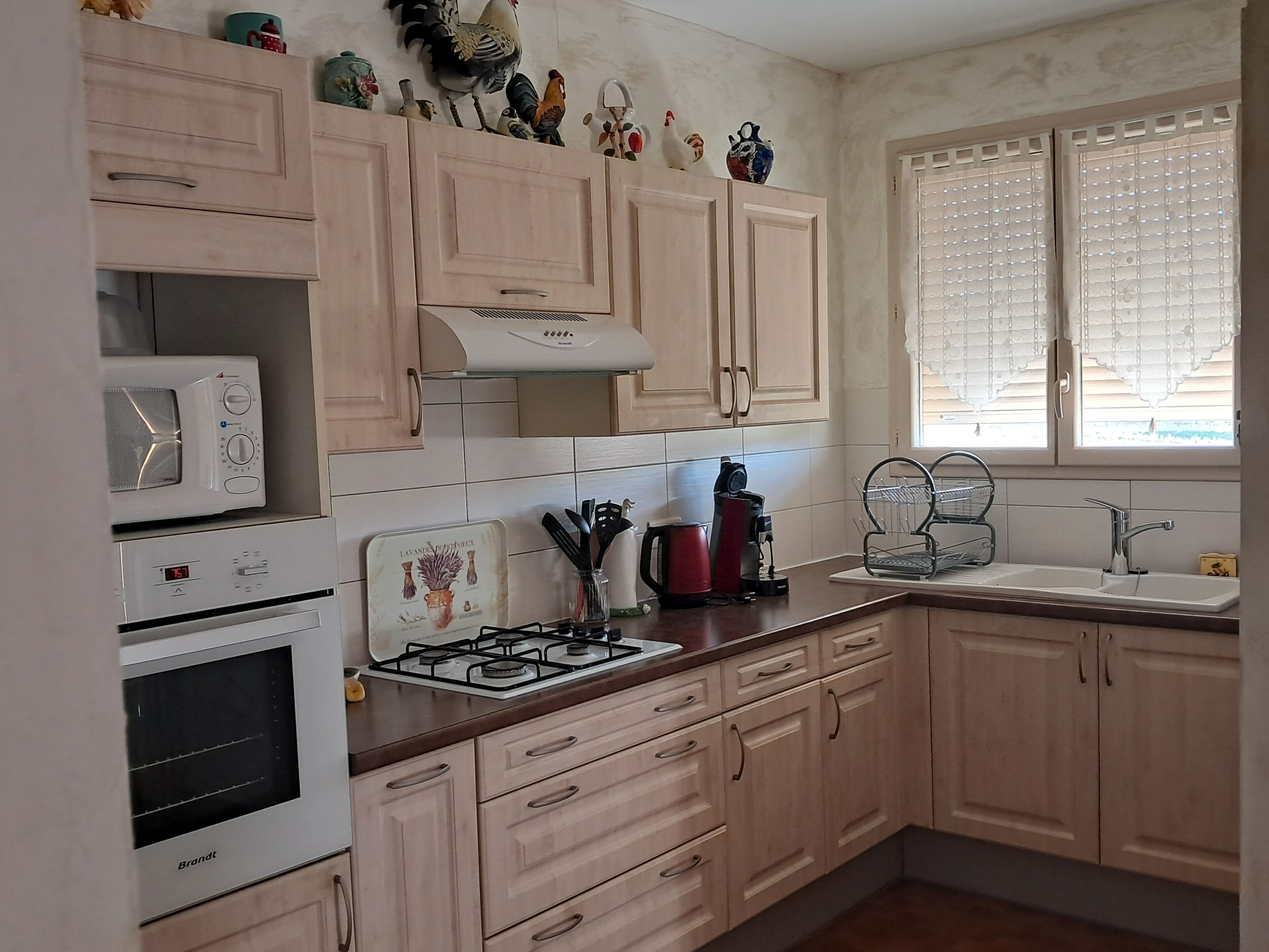 Une cuisine avec des meubles de couleur bois clair, une cuisinière à gaz, un four à micro-ondes, une bouilloire et un évier.