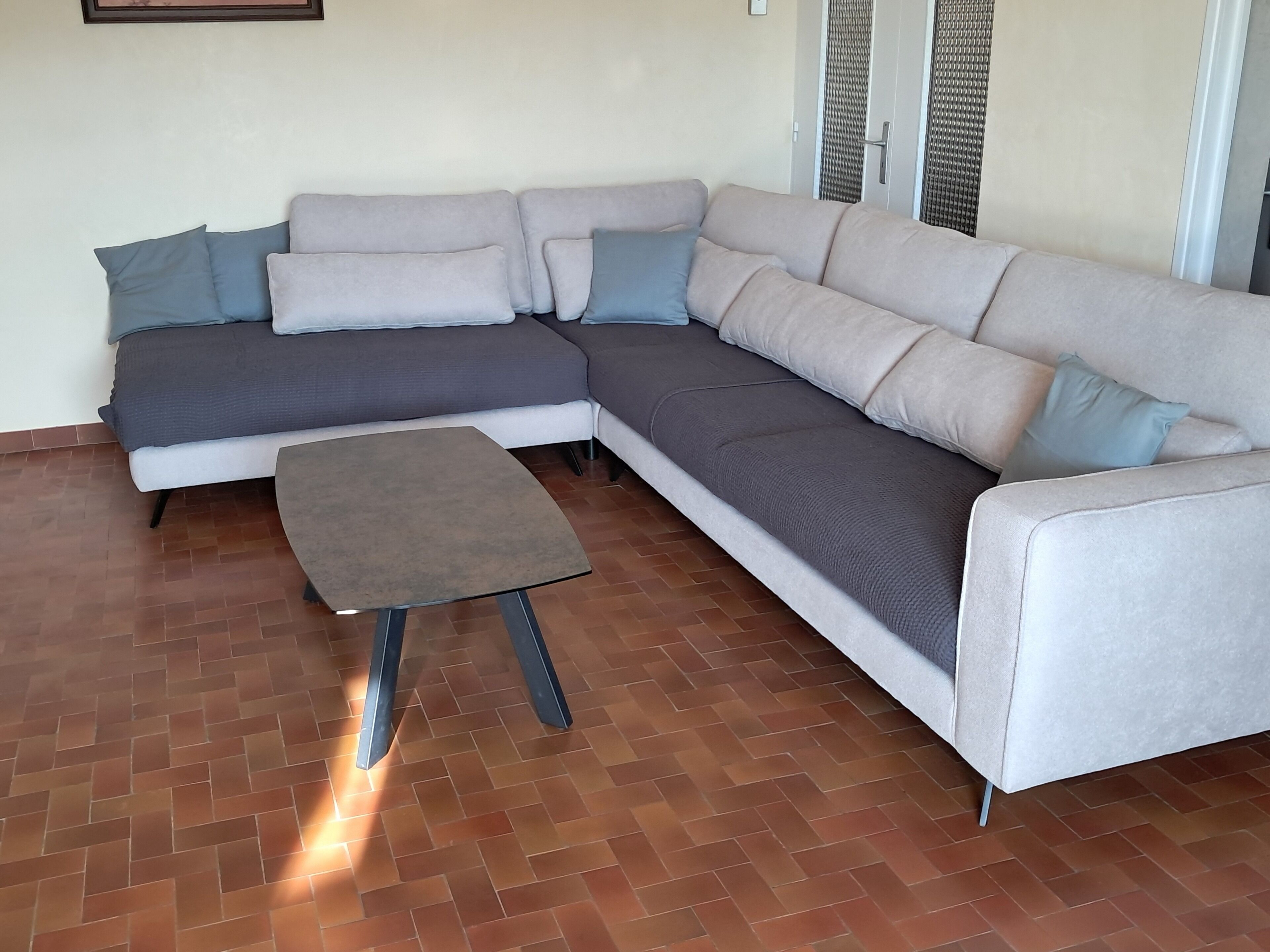 Un canapé modulable assorti d’un pouf, un parquet à motifs chevrons et une porte agrémentée d’un rideau en tissu tissé.
